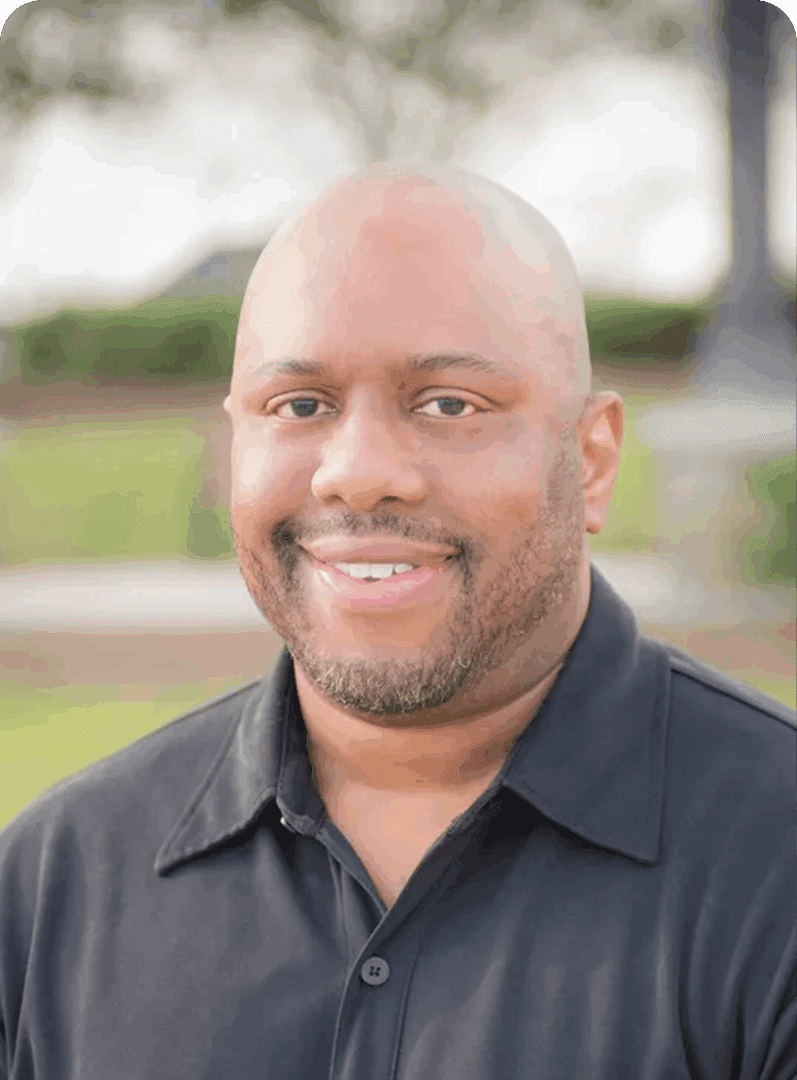 Smiling man in a black polo shirt outdoors.