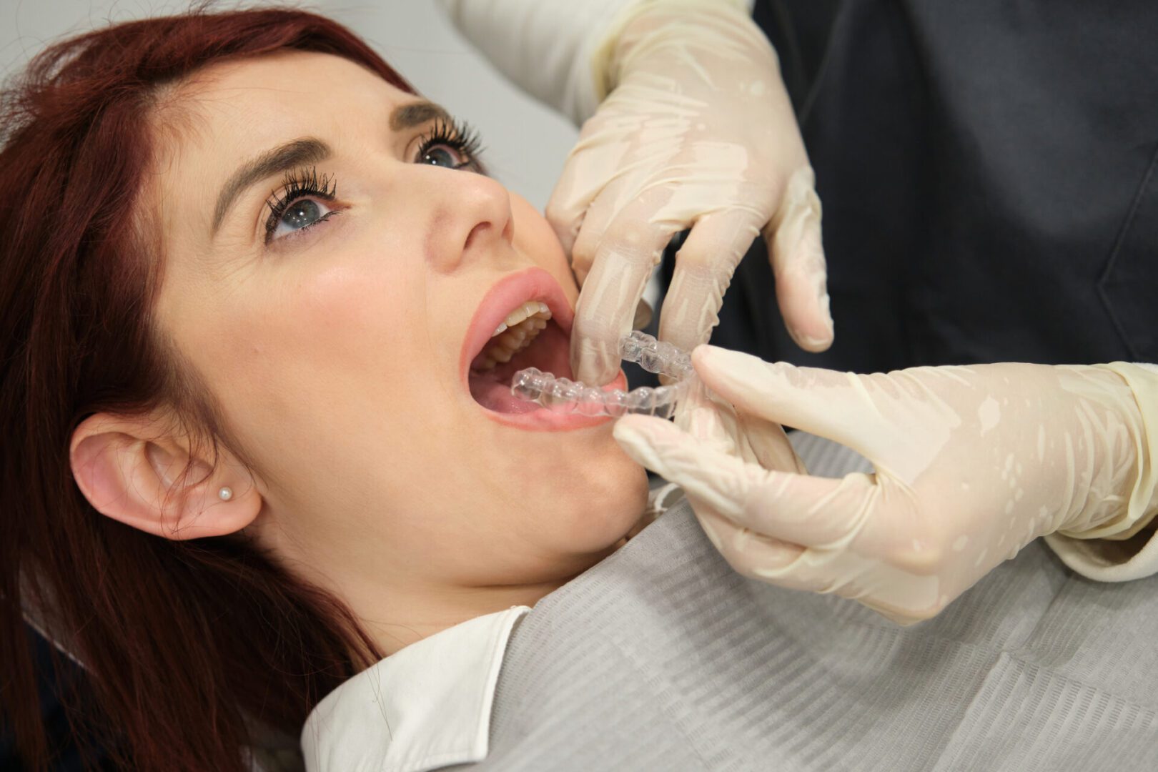 A dentist examining a patient's teeth with gloved hands.